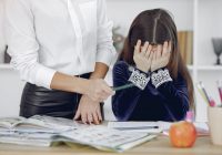 upset little girl sitting near crop woman in classroom